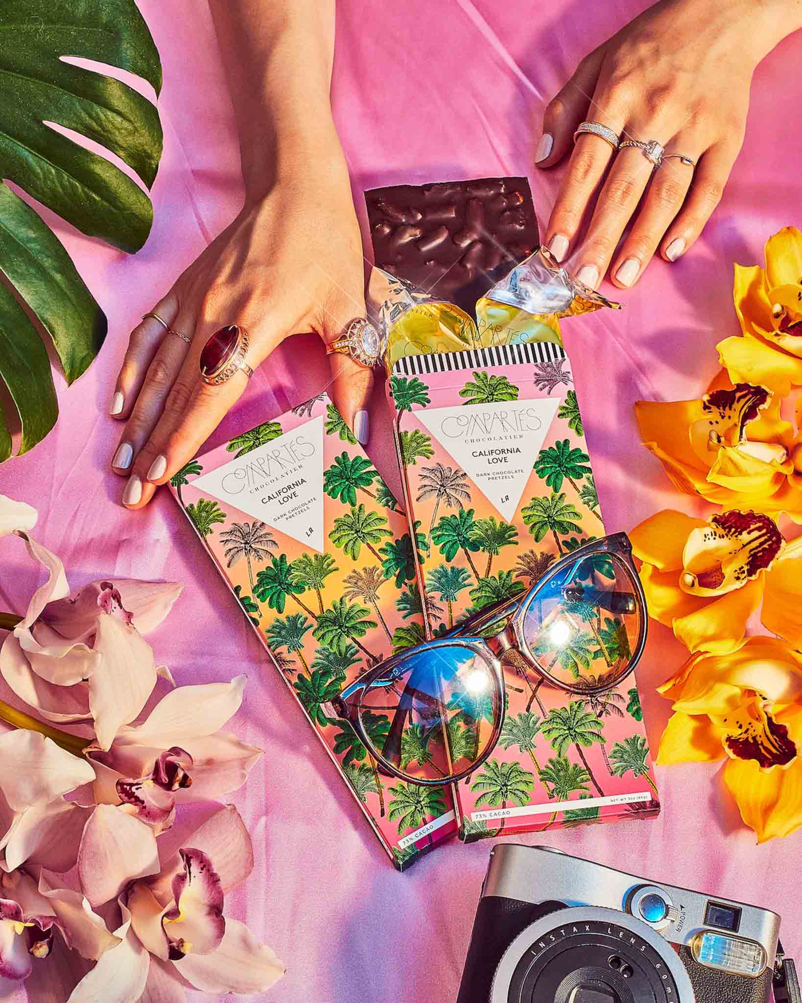 California Love Chocolate Pretzel Bar by Compartes on a colorful background with hands grabbing it